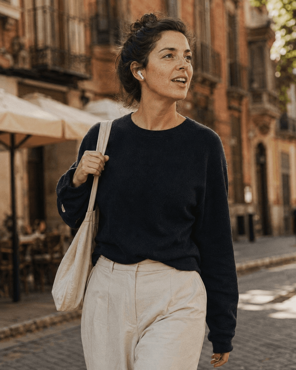 Woman walking a sunlit Spanish street with an earbud in, speaking her answer aloud